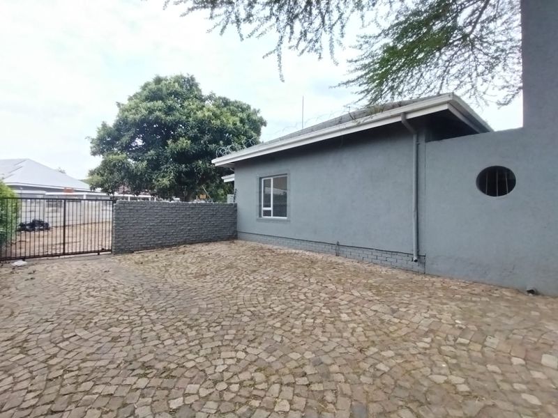 Exterior view of the property featuring a cobblestone driveway, perimeter wall with security fencing, and a side facade with a circular window.