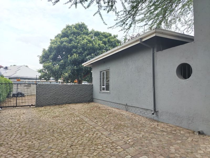 Rear exterior view of the property featuring a paved courtyard, brick boundary wall, and secure metal gate access.