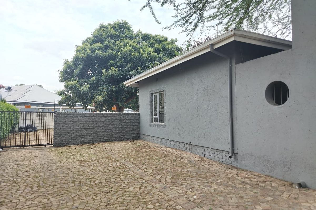 Rear exterior view of the property featuring a paved courtyard, brick boundary wall, and secure metal gate access.