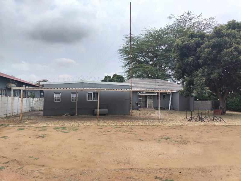 Rear view of the business property featuring a covered patio area, paved ground, and security fencing.