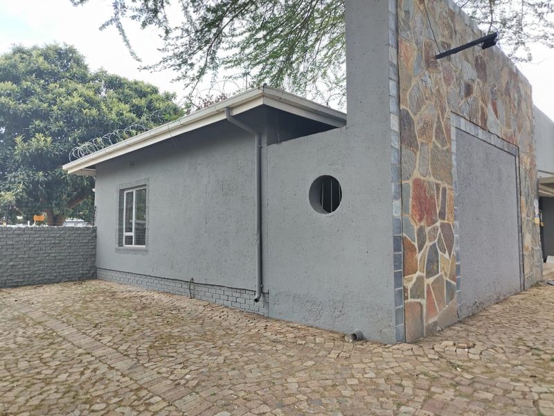 Exterior view of the property featuring stone cladding, a paved driveway, and security features including razor wire and barred windows.