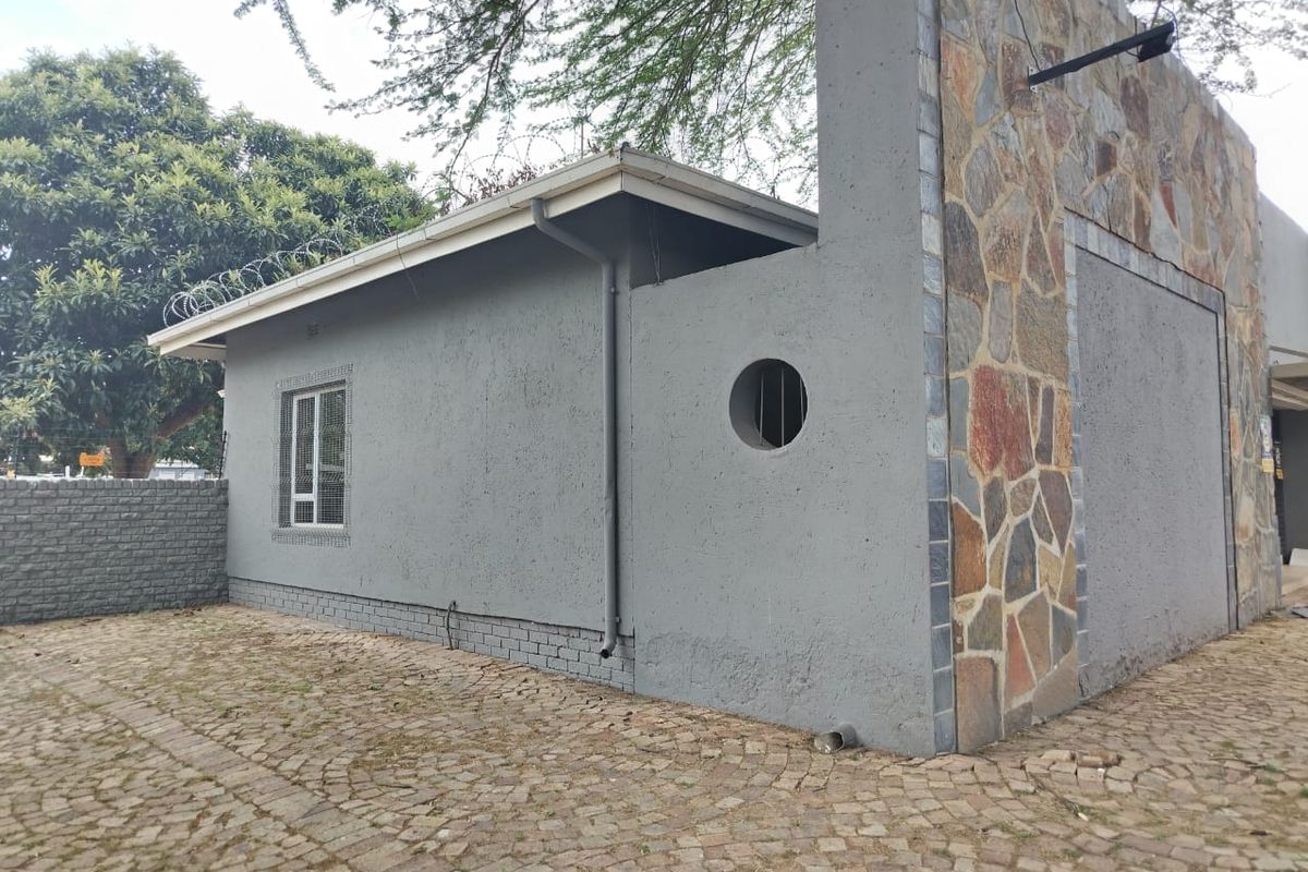 Exterior view of the property featuring stone cladding, a paved driveway, and security features including razor wire and barred windows.
