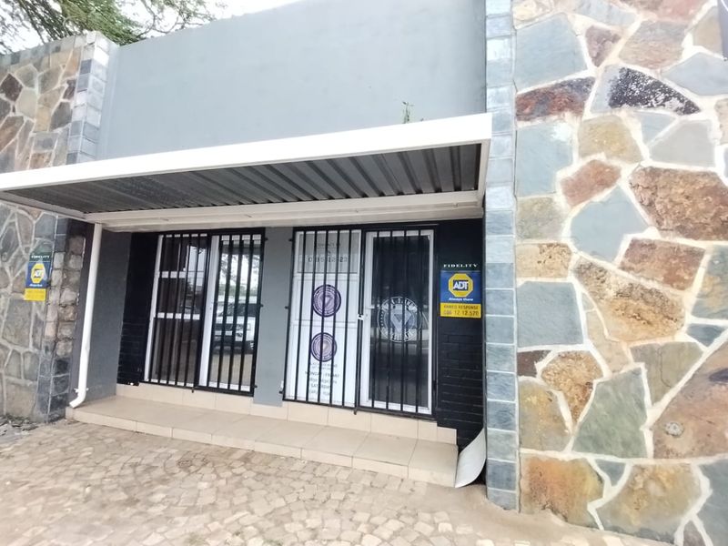 Front entrance of a commercial property featuring stone cladding, a protective metal awning, and security bars over the glass door.