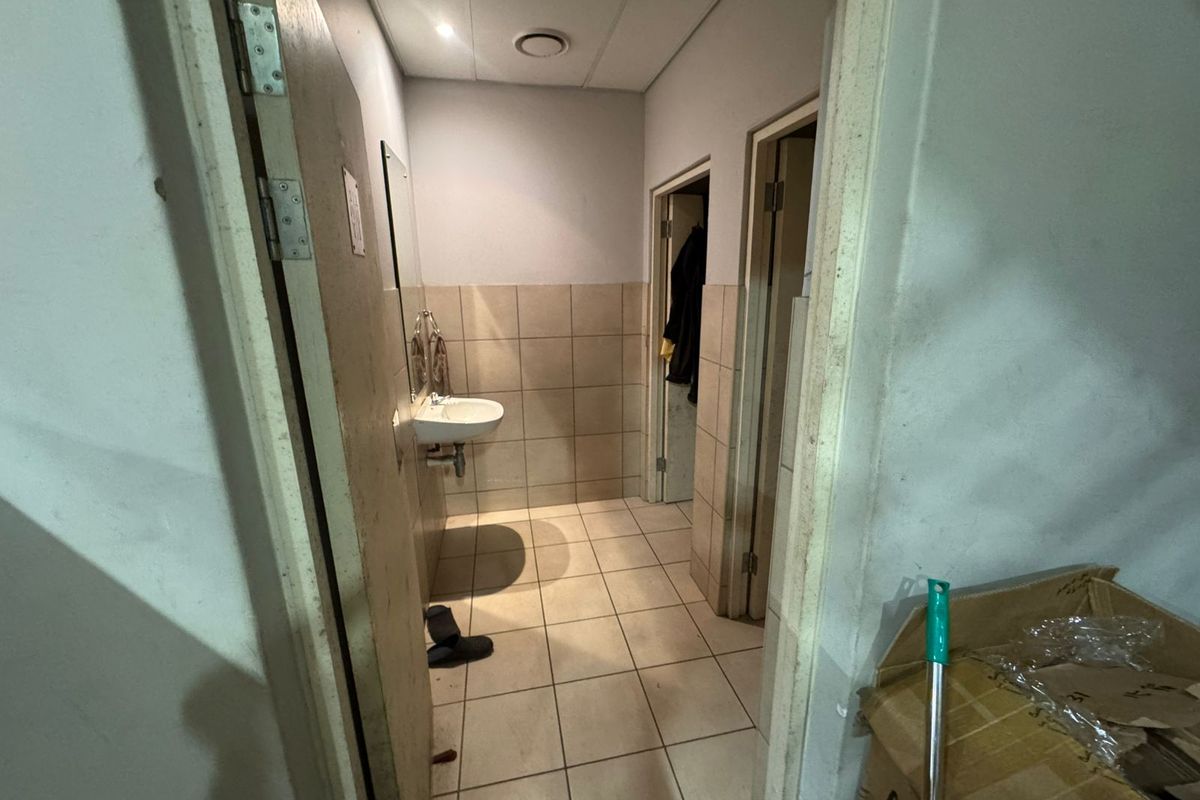 A functional industrial-style bathroom featuring a wall-mounted basin, tiled flooring, and neutral wall tiling, requiring minor cosmetic updates.