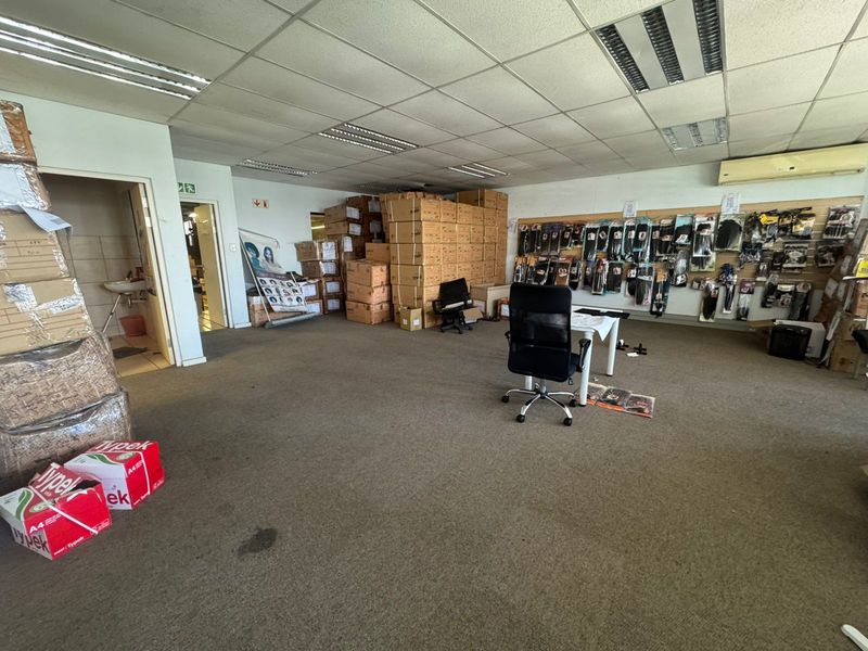 Open-plan industrial office space featuring suspended ceilings, recessed lighting, wall-mounted air conditioning, and slatwall display panels, currently utilized for storage and administrative purposes.