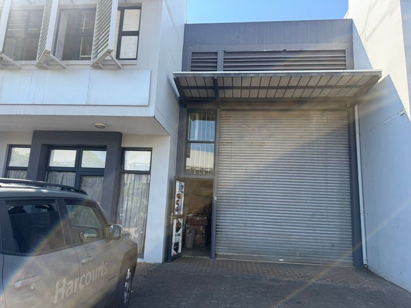 Front elevation of an industrial unit featuring a large roller shutter door, metal awning, and paved access area.
