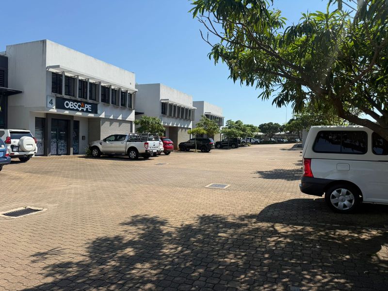 Front exterior view of an industrial business park featuring paved parking area, modern concrete facade, and secure roller shutter access points.