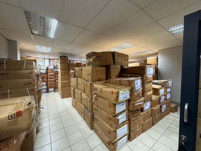 Industrial utility or storage space featuring a suspended ceiling with recessed lighting and tiled flooring, currently utilized for bulk inventory storage.