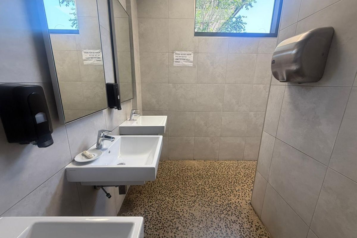 A clean, modern industrial-style bathroom featuring wall-mounted ceramic basins, chrome fixtures, tiled walls, and durable exposed aggregate flooring.