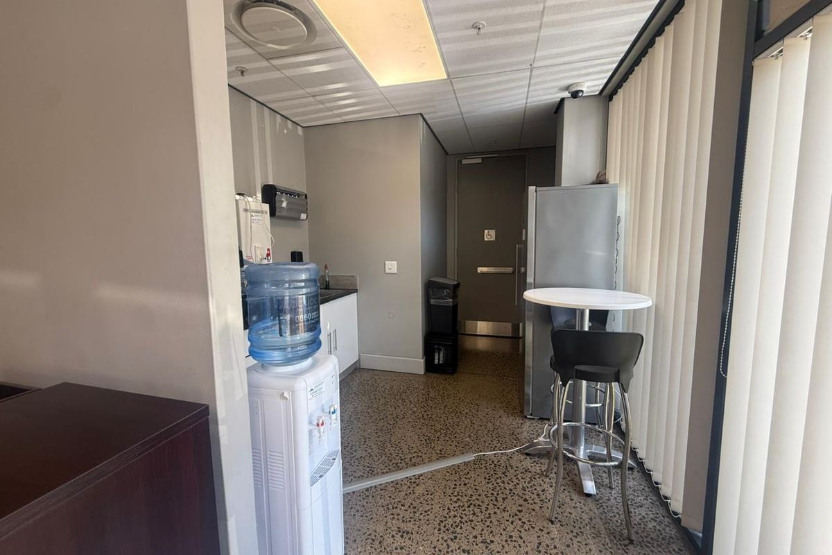 A functional industrial kitchenette featuring built-in cabinetry, a sink, drop ceiling with recessed lighting, and durable exposed aggregate flooring.