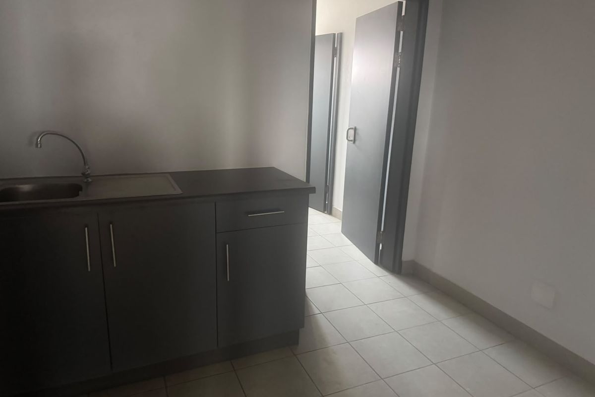 A functional kitchenette area featuring dark cabinetry, a stainless steel sink, and tiled flooring, leading into a hallway with additional internal doors.