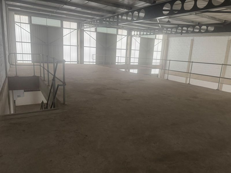 An open-plan industrial mezzanine level featuring steel support beams, metal safety railings, and translucent wall panels, providing versatile storage or workspace potential.
