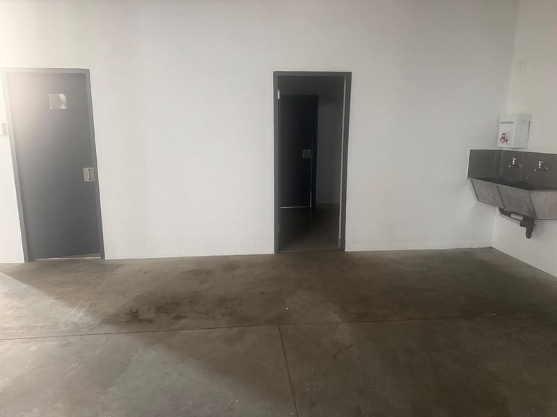 A functional industrial utility space featuring concrete flooring, two internal access doors, and a wall-mounted stainless steel industrial sink.