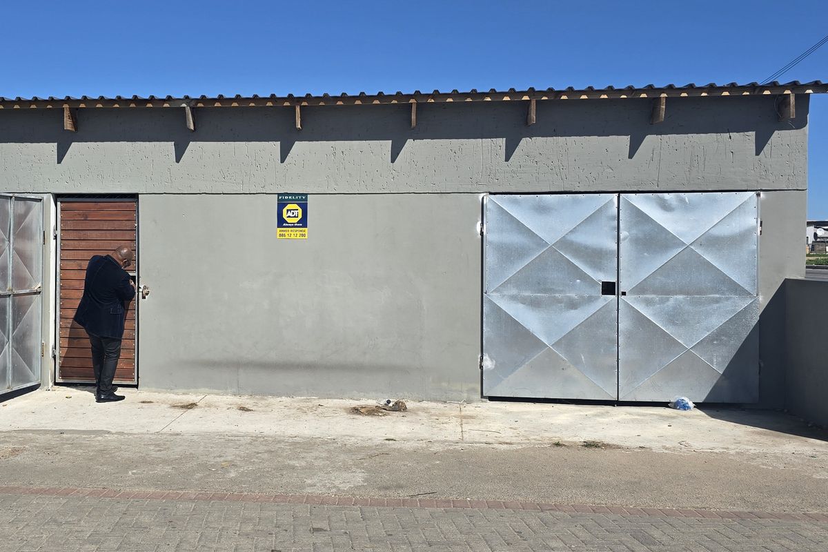 Exterior view of a functional garage structure featuring metal double doors and a security gate, situated on a concrete apron.