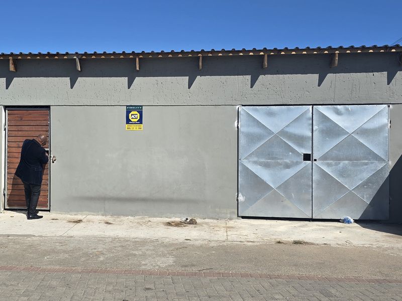 Exterior view of a functional garage structure featuring metal double doors and a security gate, situated on a concrete apron.