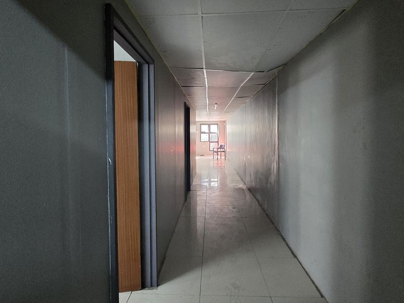 A long, empty commercial hallway featuring tiled flooring and a suspended ceiling, showing signs of wear and requiring cosmetic updates.