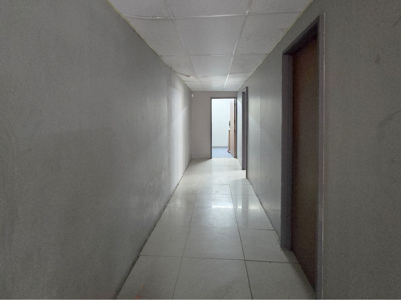 A vacant commercial hallway featuring tiled flooring, a suspended ceiling, and multiple internal access doors.