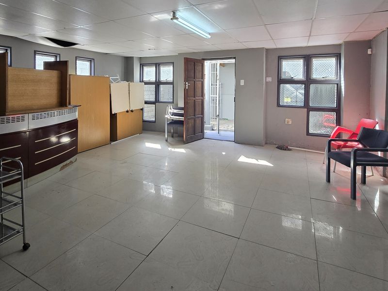 A functional office space featuring tiled flooring, a built-in reception counter, and security-fitted windows, offering a versatile layout for business operations.