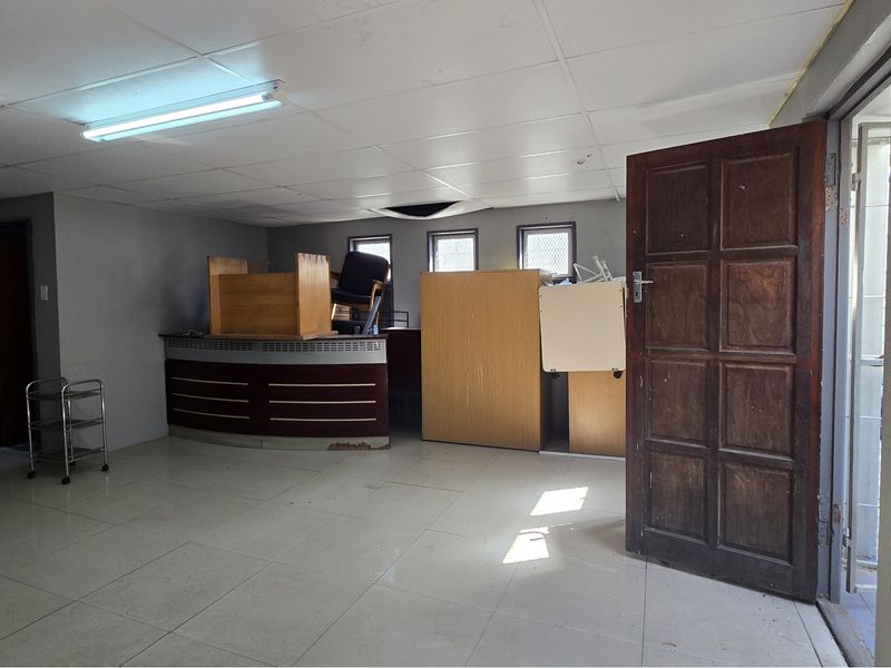 An office space featuring tiled flooring, a drop ceiling with fluorescent lighting, and a timber entrance door.