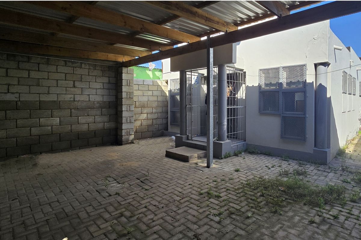 A paved rear courtyard area featuring a timber-framed covered section, security gates, and perimeter block walling, requiring some maintenance and landscaping.