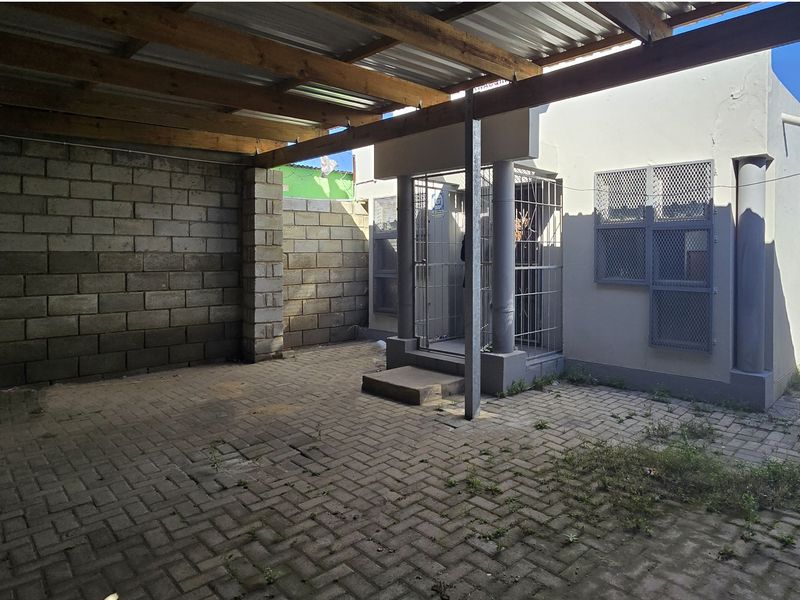 A paved rear courtyard area featuring a timber-framed covered section, security gates, and perimeter block walling, requiring some maintenance and landscaping.