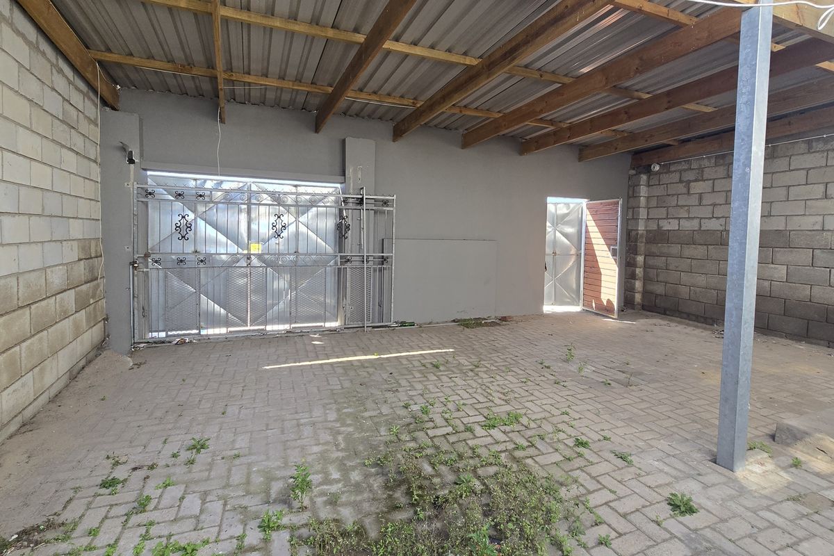 An open-sided garage or utility space featuring paved flooring, concrete block walls, and a corrugated metal roof with exposed timber rafters.
