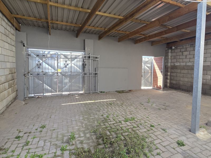 An open-sided garage or utility space featuring paved flooring, concrete block walls, and a corrugated metal roof with exposed timber rafters.