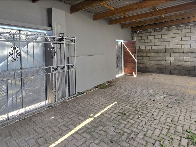 A functional, open-style garage or utility space featuring paved flooring, exposed timber rafters, and secure metal gate access.