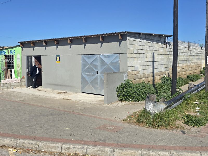 Street-level view of a commercial property featuring a concrete block structure with a metal garage door and perimeter security fencing.
