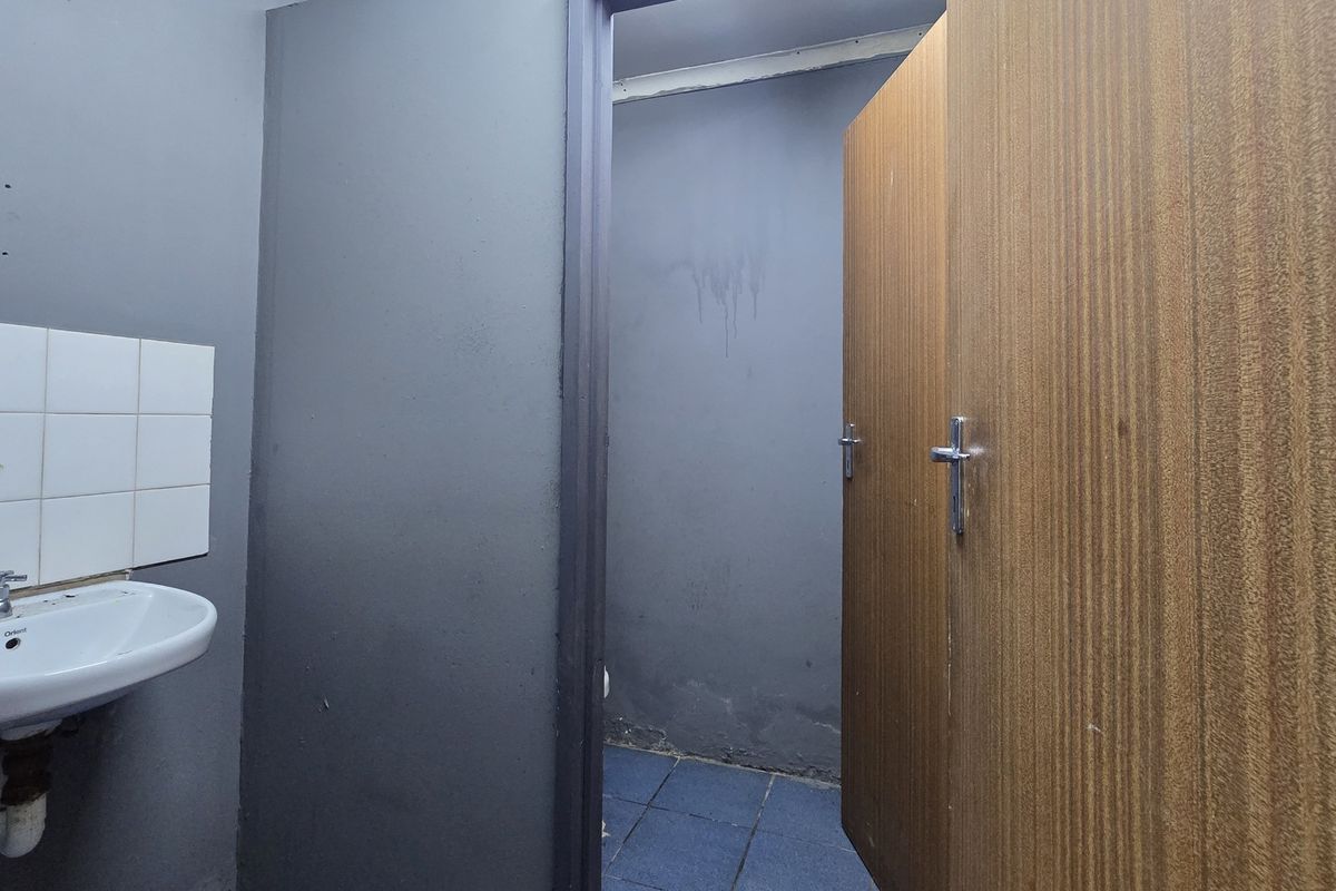A small bathroom featuring a wall-mounted basin with tiled splashback, blue floor tiles, and a wooden door, requiring cosmetic updates and wall repairs.