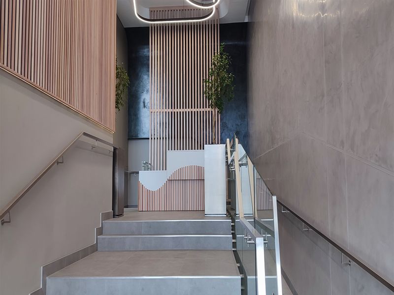 Modern office entrance featuring a stylish staircase with glass balustrades, contemporary slatted timber wall accents, and a sleek reception area with high-end finishes.