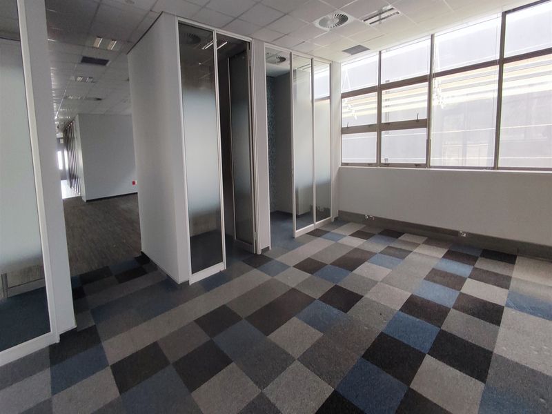 A bright, vacant office space featuring modern glass partitions, suspended ceilings with recessed lighting, and patterned carpet tiles, offering a clean professional environment.