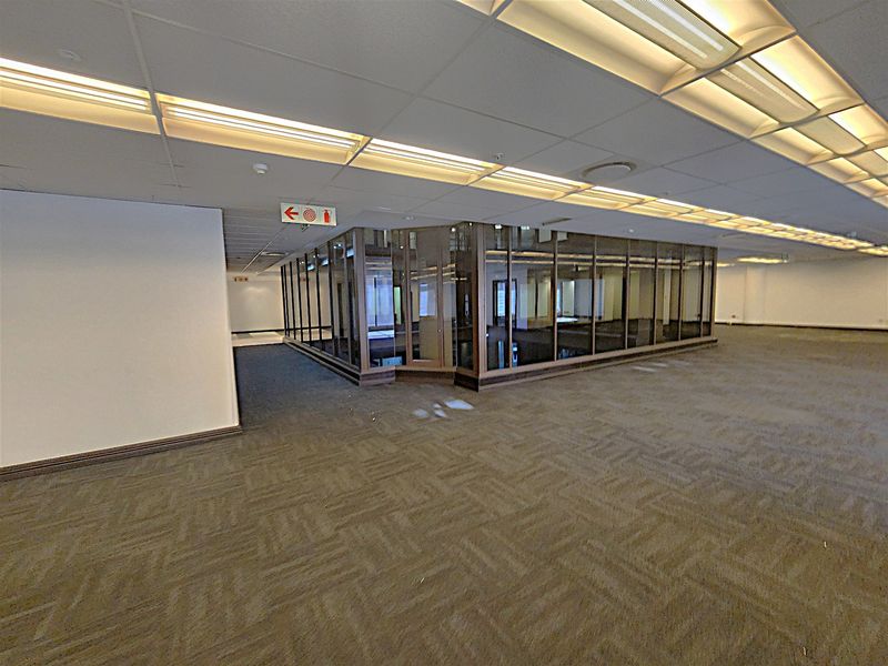 Spacious open-plan office area featuring glass-partitioned meeting rooms, suspended ceilings with recessed lighting, and neutral carpeting throughout.