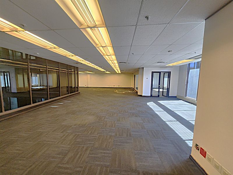 Spacious open-plan office area featuring suspended ceilings, fluorescent lighting, carpeted flooring, and glass partition walls, offering a versatile workspace layout.