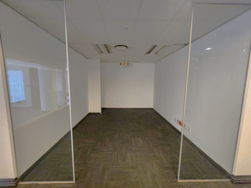 A vacant office space featuring glass partition walls, carpeted flooring, and a suspended ceiling with integrated lighting, suitable for a professional work environment.
