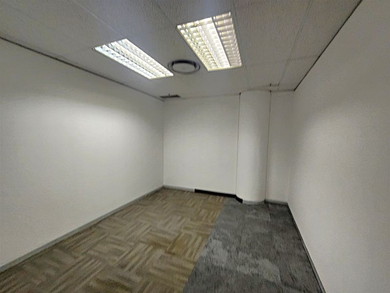 An empty office space featuring a suspended ceiling with recessed lighting, a structural column, and mixed carpet tile flooring.