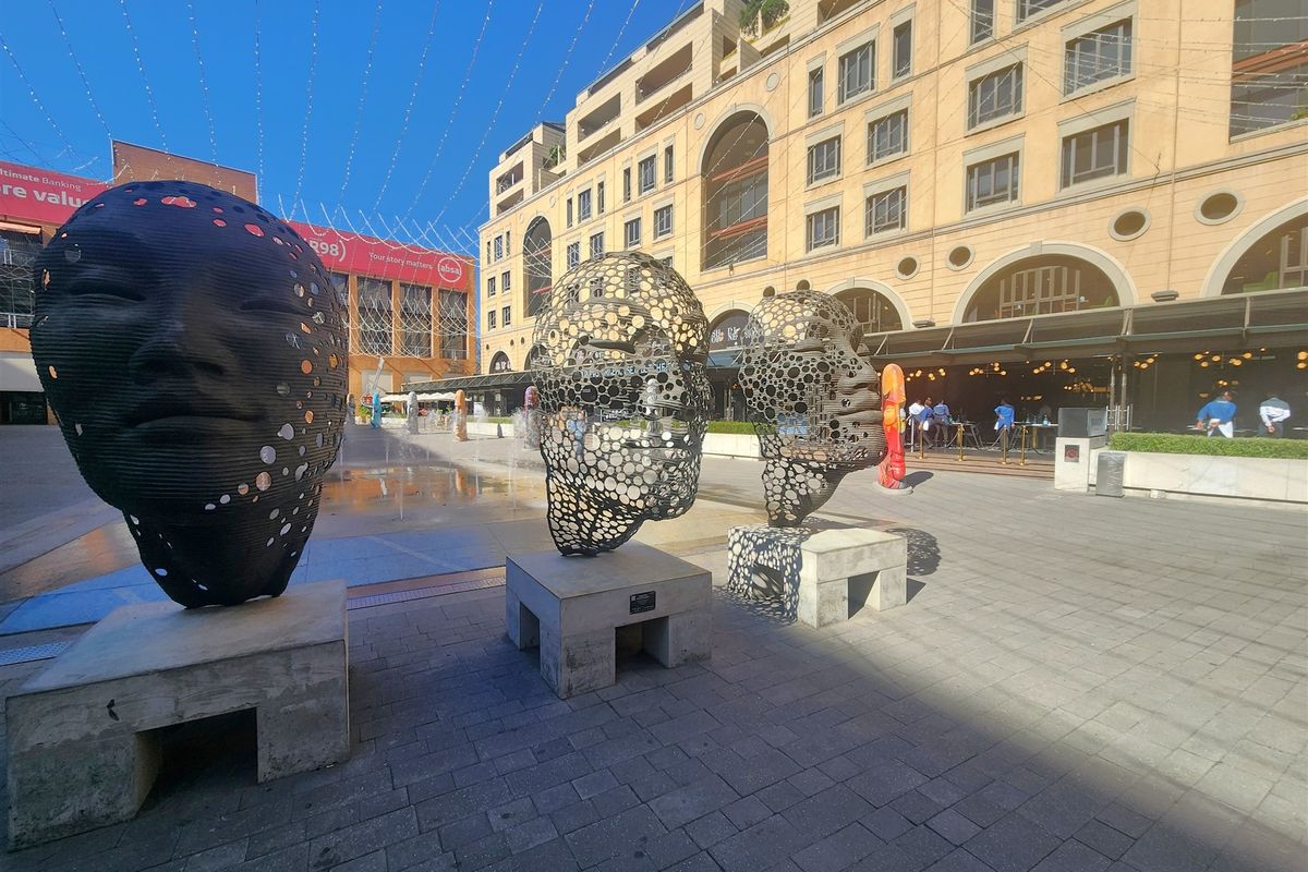 A view of a modern commercial office building exterior featuring a paved plaza and decorative sculptural installations.