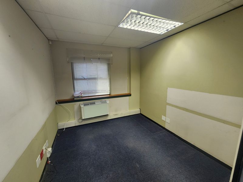 An empty office space featuring a suspended ceiling, recessed lighting, wall-mounted air conditioning, and carpeted flooring, ready for professional fit-out.