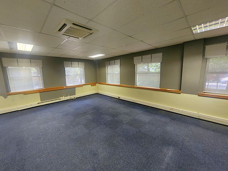 An empty office space featuring a suspended ceiling, recessed lighting, cassette air conditioning, perimeter trunking, and large windows with fitted blinds.