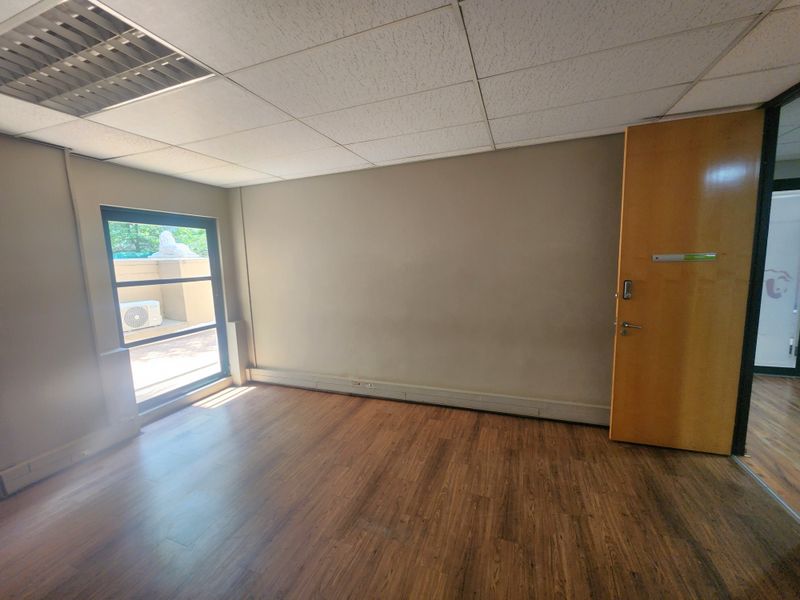 A vacant office space featuring laminate flooring, a suspended ceiling with recessed lighting, and a timber door, offering a clean canvas for professional use.