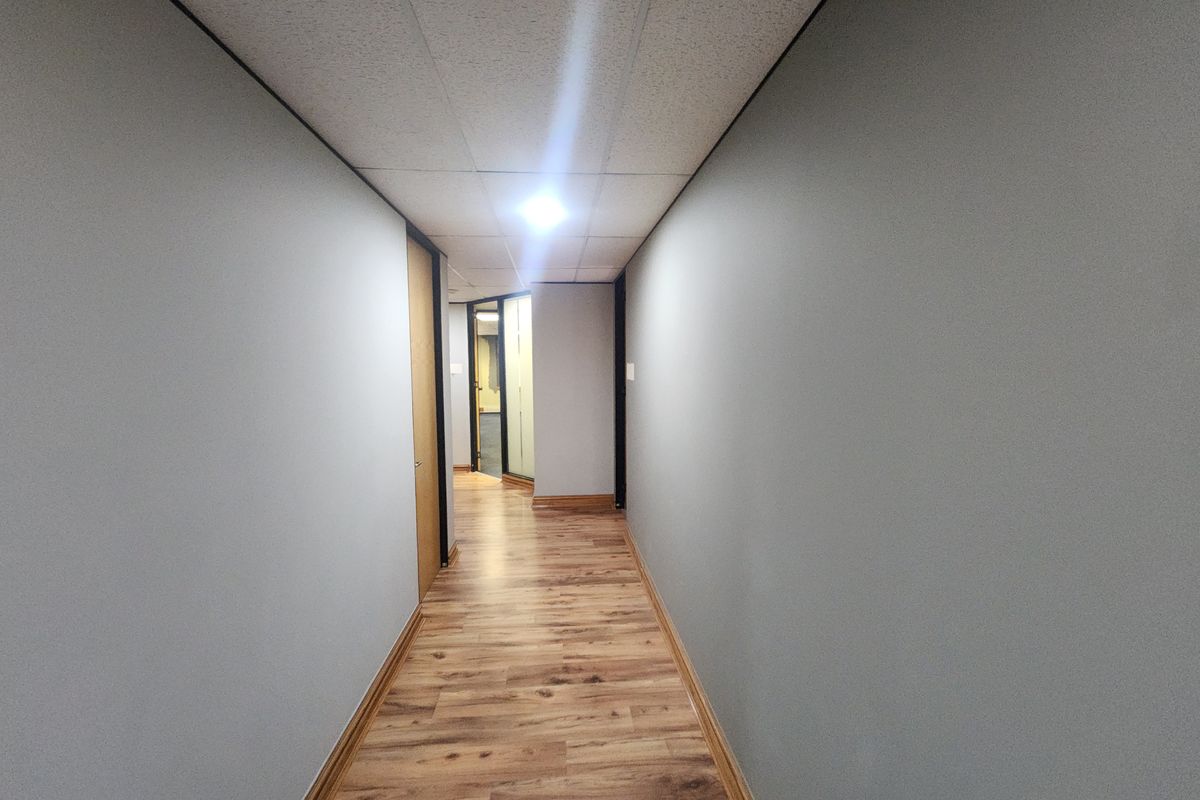 A clean, well-maintained office hallway featuring modern laminate flooring, neutral grey walls, and a suspended ceiling with recessed lighting.