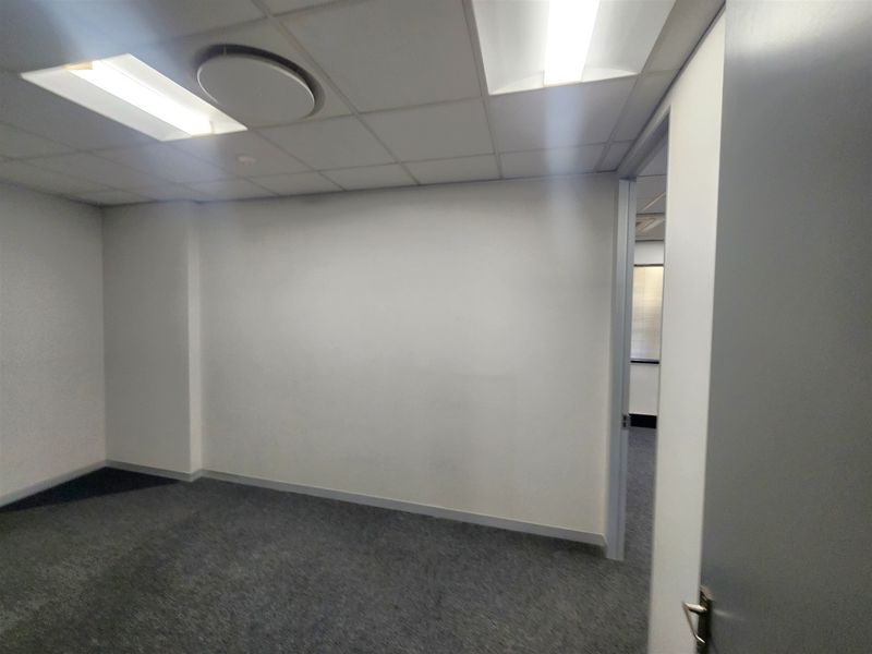 A vacant office space featuring a suspended ceiling with recessed lighting and carpeted flooring, offering a clean and functional workspace environment.