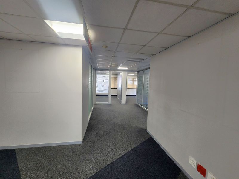 A clean, empty office hallway featuring suspended ceilings, recessed lighting, and glass partition walls leading to private office spaces.