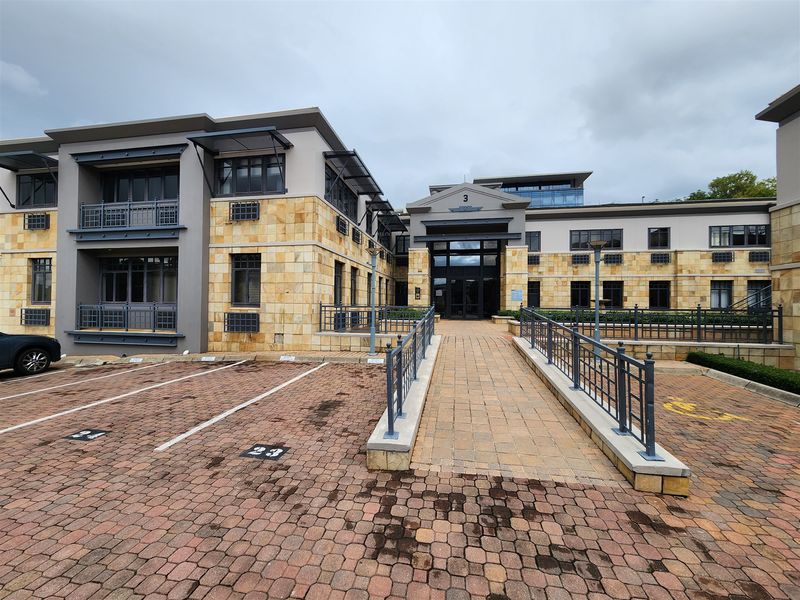 Front exterior view of a modern office building featuring stone cladding, a paved pedestrian ramp, and dedicated parking bays.