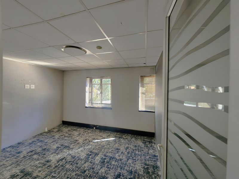 An empty office space featuring a suspended ceiling, recessed lighting, patterned carpet flooring, and a modern frosted glass door.