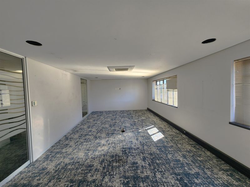 A vacant office space featuring patterned carpeting, recessed ceiling lighting, ducted air conditioning, and a glass partition wall with natural light from side windows.