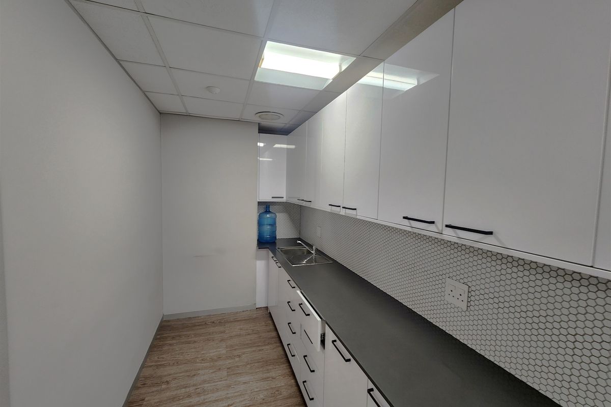 A clean, modern office kitchenette featuring white cabinetry, dark countertops, a stainless steel sink, and a stylish hexagonal tile backsplash.