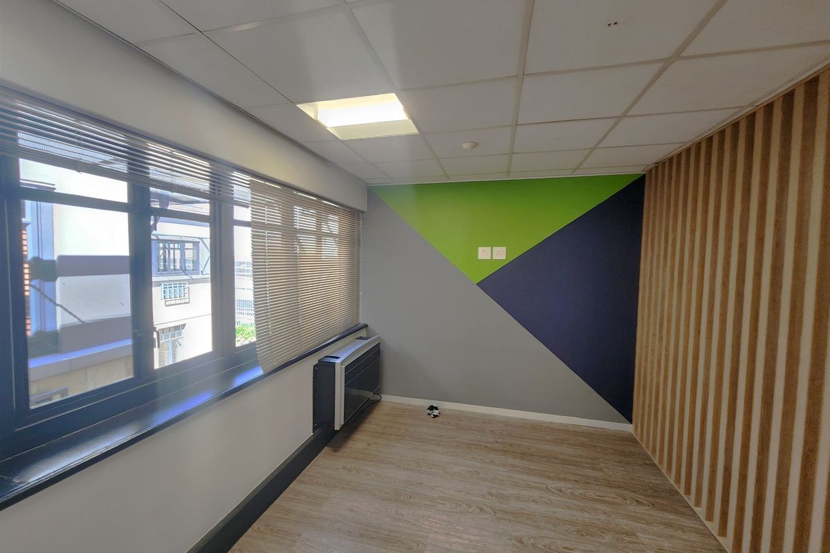 A bright, modern office space featuring wood-look flooring, slatted wood accent wall, suspended ceiling, and a wall-mounted air conditioning unit.