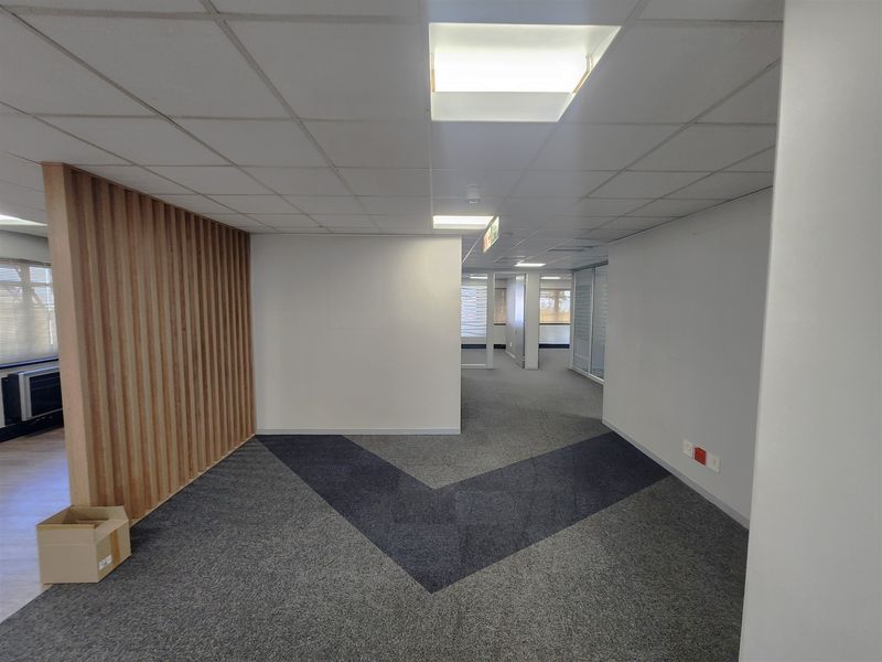 A modern, open-plan office space featuring a timber slat accent wall, suspended ceiling with recessed lighting, and patterned carpet flooring.