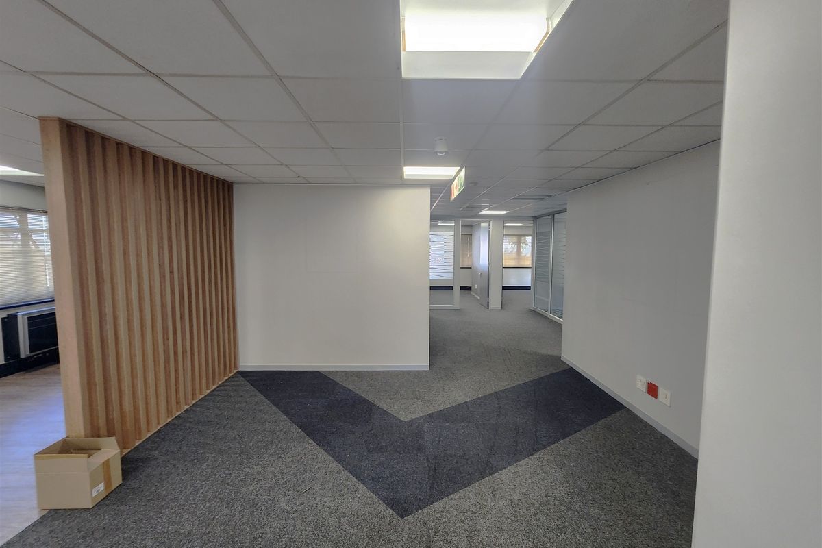 A modern, open-plan office space featuring a timber slat accent wall, suspended ceiling with recessed lighting, and patterned carpet flooring.